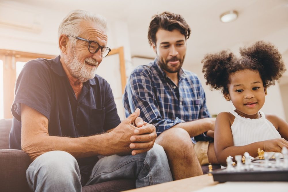 Grandfather and father watching daughter play chess