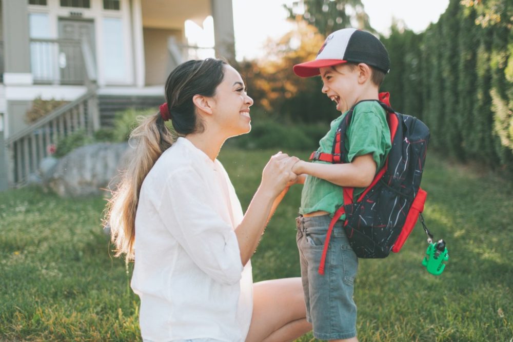 Mother and son with backpack smiling on the way to school